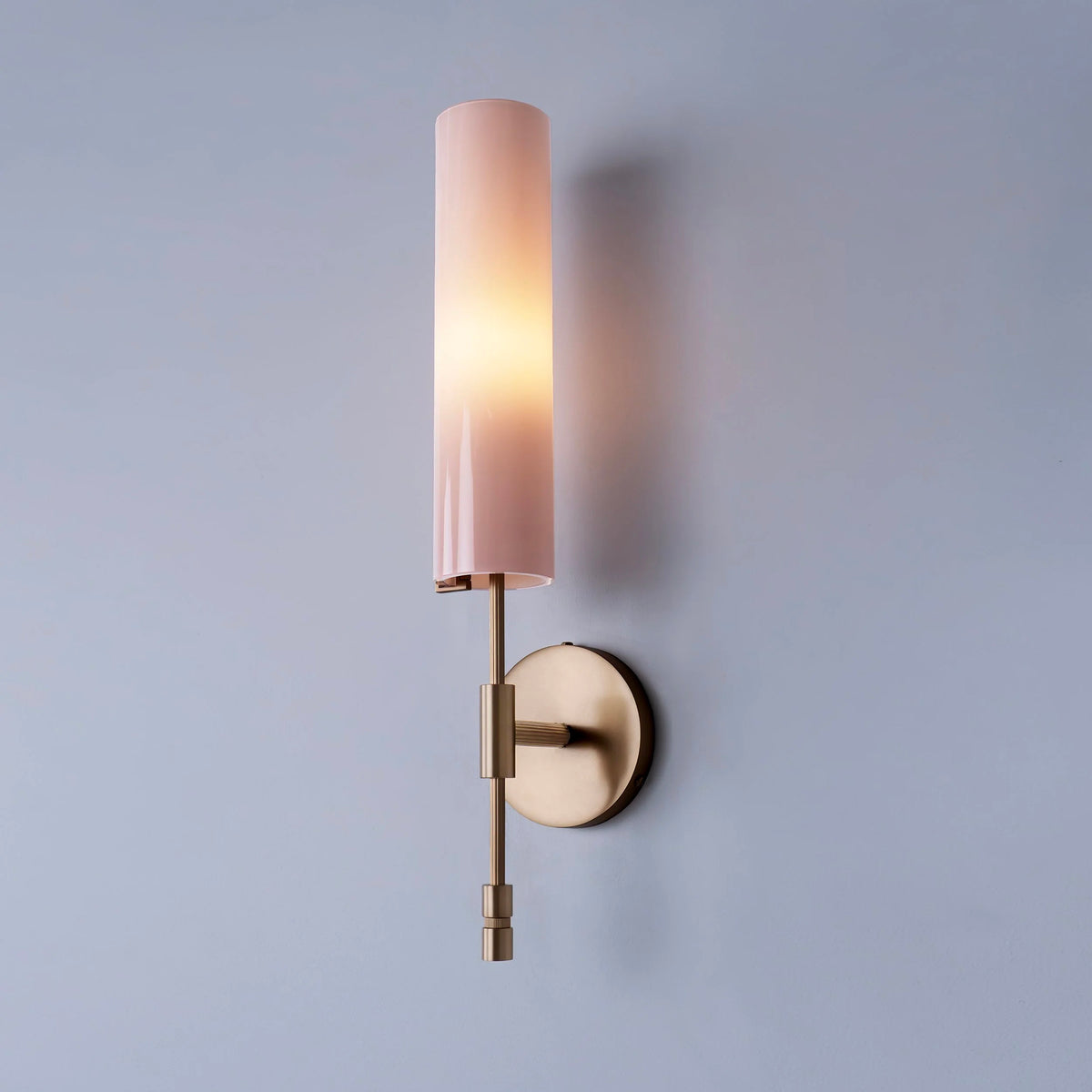 Glossy pink glass wall-mounted sconce with cylindrical shade and brass wall attachment.