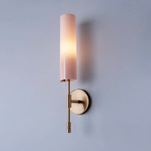 Glossy pink glass wall-mounted sconce with cylindrical shade and brass wall attachment.