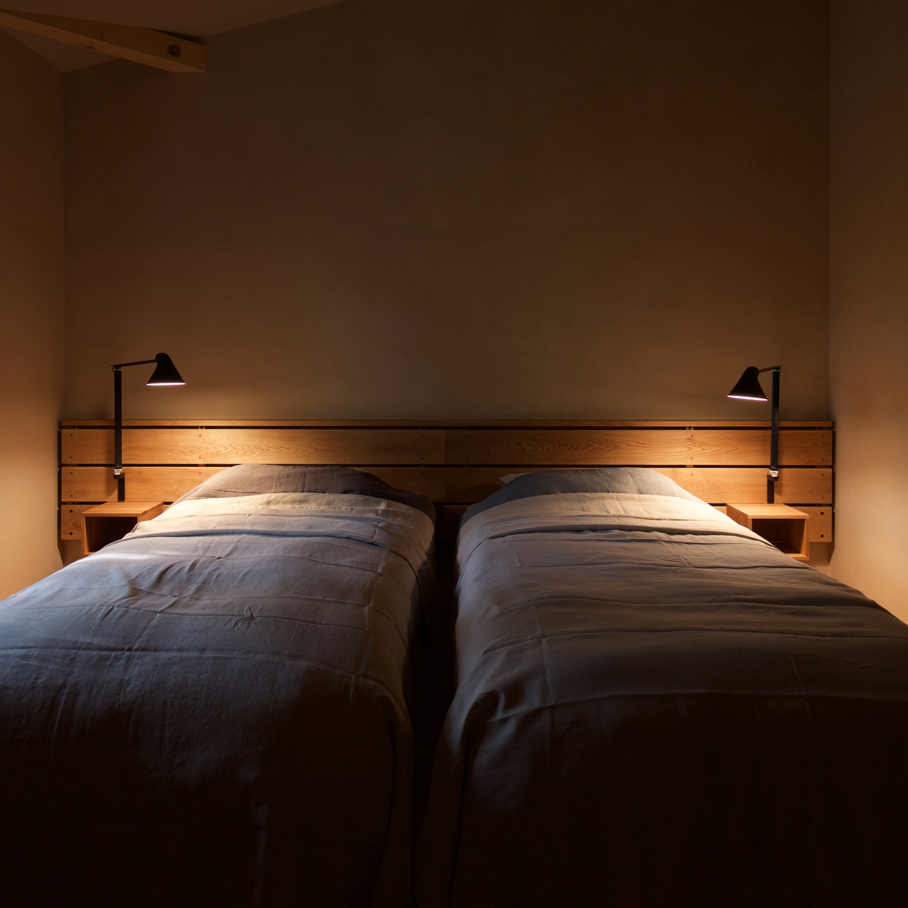 NJP wall lamps with long arms in black by Louis Poulsen, mounted on both sides of a bed in a modern bedroom setting for balanced lighting